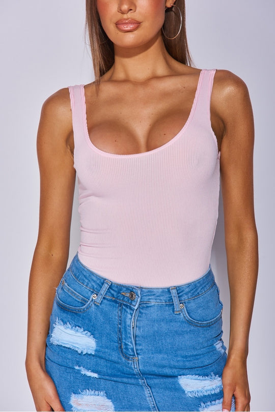 Close up of the models torso. Model weras pink ribbed bodysuit with scoop neck detailing. Model wears a blue denim skirt. Model stands ith her hands to the side. 