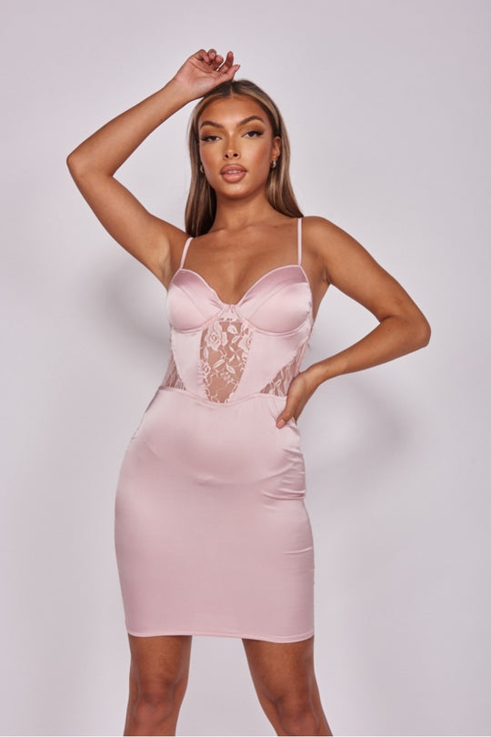 Model wears pink satin dress with front lace panel detailing with cup detailing.  Model faces the camera, she places one had on her hip and the other above her head.