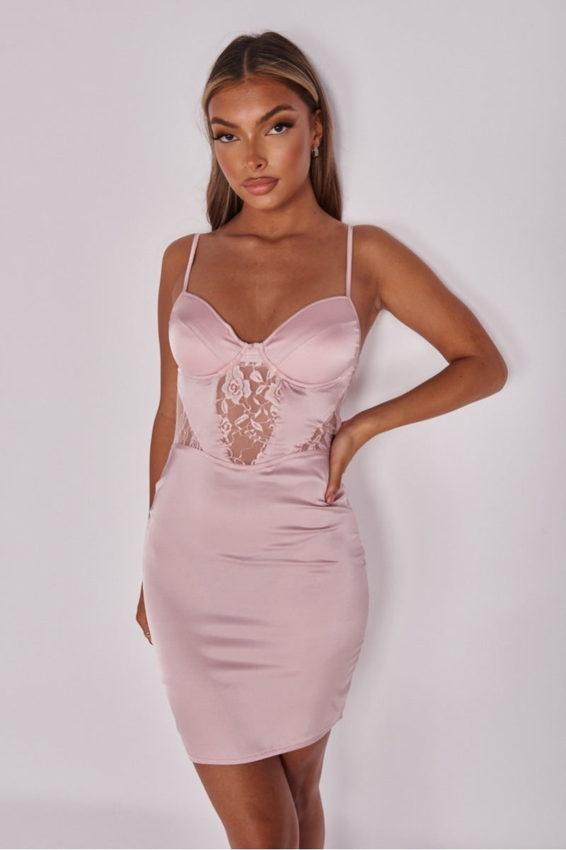 Model wears pink satin dress with front lace panel detailing with cup detailing. Model faces the camera and has one hand on her hip and one behind her hip.