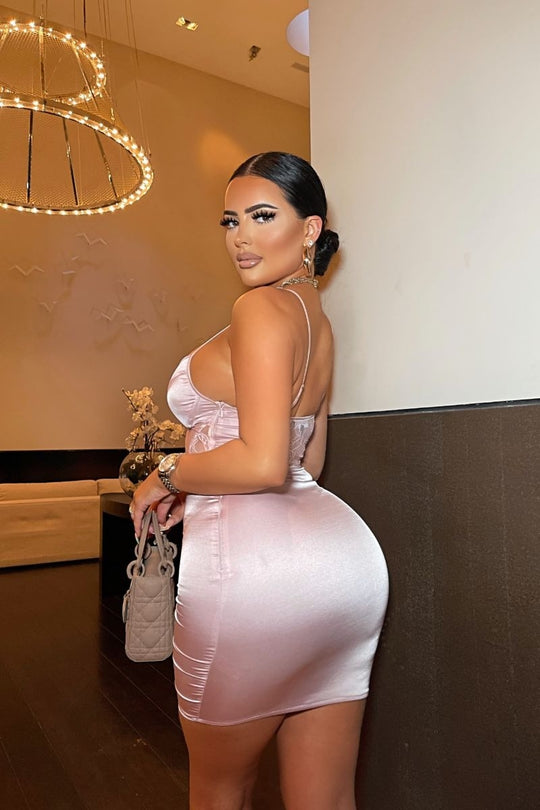 Model wears pink satin dress with front lace panel detailing with cup detailing.  Model stands with her back to the camera. The back of the dress is visible.